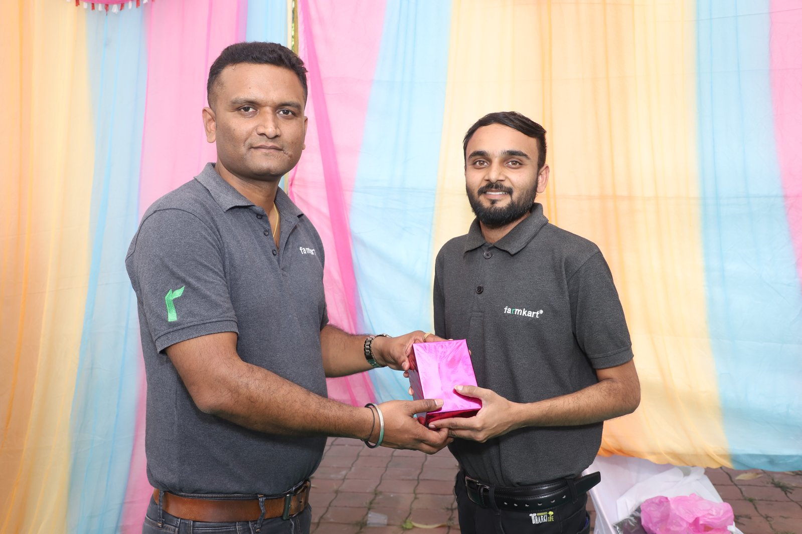 Two farmkart team members exchange a gift in branded polos at Kelratn